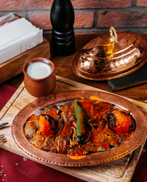 Premium sliced meat in tomato sauce served on a copper platter at Layali Riyadh, with grilled tomatoes and a side of fresh ayran yogurt drink